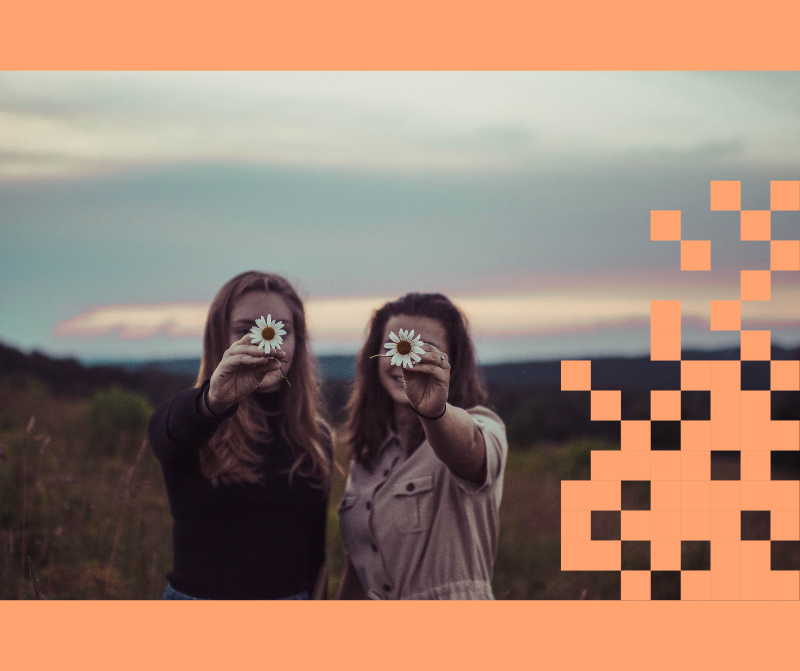 Kaksi tyttöä hämärtyvällä niityllä, pitävät päivänkakkaroita kasvojensa edessä.