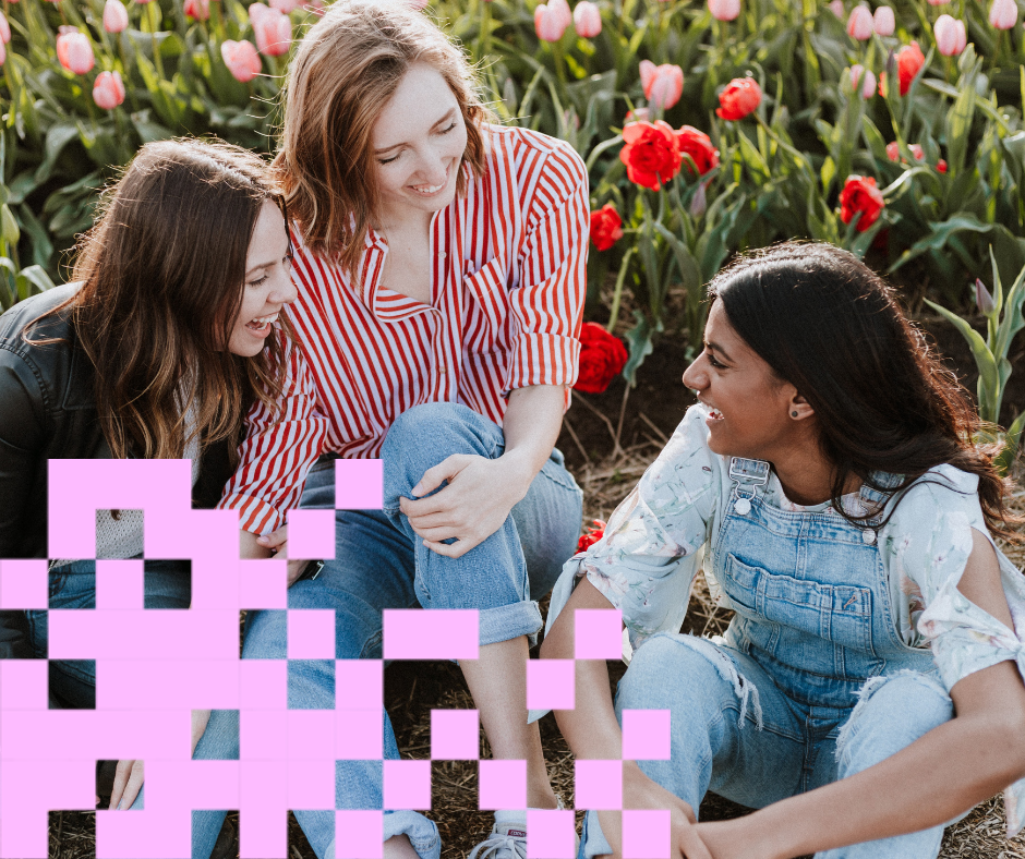 Kolme nuorta naista juttelee niityllä, vaaleanpunaiset pikselit kulmassa