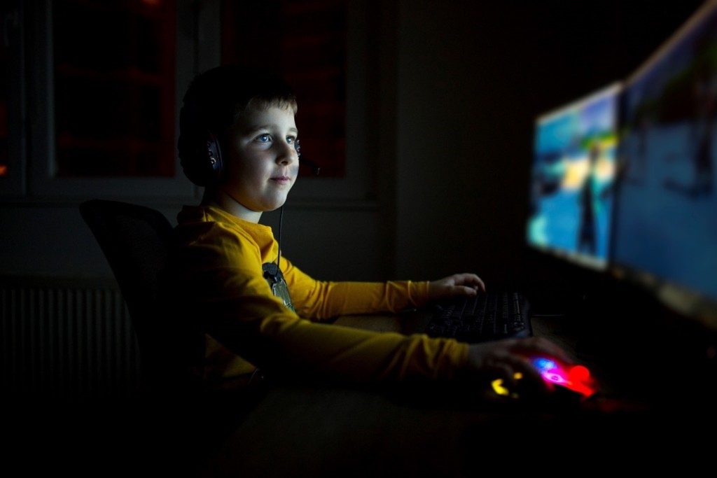 Poika pelaamassa tietokoneella pimeässä huoneessa.